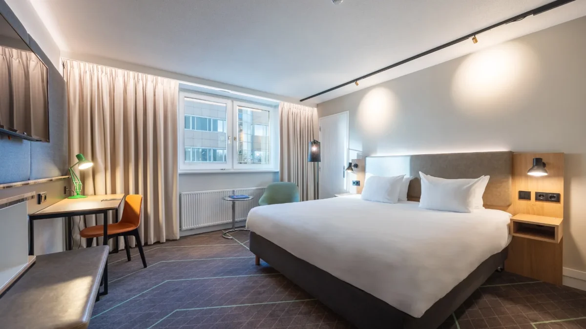 Room with a king size bed, desk and a view over the city